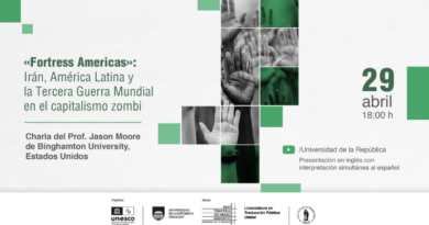 Imagen horizontal con fondo claro (blanco grisáceo) y una estética limpia con acentos en verde. En el lado izquierdo, ocupa la mitad del espacio un bloque de texto en verde oscuro que dice: “«Fortress Americas»: Irán, América Latina y la Tercera Guerra Mundial en el capitalismo zombi”. Debajo, separado por una línea fina verde, aparece en gris: “Charla del Prof. Jason Moore de Binghamton University, Estados Unidos”. En el centro hay una composición visual formada por una grilla de rectángulos verticales y horizontales. Dentro de ellos se ven fotografías en blanco y negro de manos levantadas (palmas abiertas hacia el frente), algunas intervenidas con filtros verdes translúcidos. Los rectángulos están intercalados con bloques planos de color verde en distintos tonos, generando un patrón geométrico. A la derecha, sobre fondo claro, se destaca la fecha en tipografía grande verde: “29”, y debajo en gris: “abril” y “18:00 h”. Más abajo aparece un ícono de Youtube seguido de “/Universidad de la República” y en gris: “Presentación en inglés con interpretación simultánea al español”. En la parte inferior, sobre una franja clara, se alinean varios logos institucionales en escala de grises, incluyendo UNESCO, Universidad de la República, Red Temática de Medio Ambiente, Licenciatura en Traducción Pública y Facultad de Derecho. Pequeños cuadrados verdes distribuidos en distintos puntos del fondo refuerzan la composición visual.