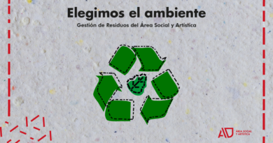 La imagen presenta un diseño horizontal con fondo de textura similar a papel reciclado, en tonos gris claro, lo que refuerza una estética ecológica y artesanal. En la parte superior, centrado, aparece el texto en negro: “Elegimos el ambiente”, en tipografía grande y negrita. Debajo, en un tamaño menor, se lee: “Gestión de Residuos del Área Social y Artística”. En el centro de la composición hay un símbolo de reciclaje formado por seis figuras verdes irregulares que simulan flechas, dispuestas en forma circular. Estas piezas tienen un contorno punteado negro, lo que les da un estilo gráfico más manual o intervenido. En el medio del círculo hay una forma verde más pequeña, también con contorno punteado. Toda la imagen está enmarcada por una línea roja discontinua que recorre el borde interior, como si fuera un recorte o troquel. En la esquina inferior izquierda aparecen pequeños fragmentos de líneas rojas dispersas, como restos de ese mismo trazo. En la esquina inferior derecha se encuentra el logo en rojo del Área Social y Artística, con las siglas “AD” destacadas y el texto “Área Social y Artística” en menor tamaño.
